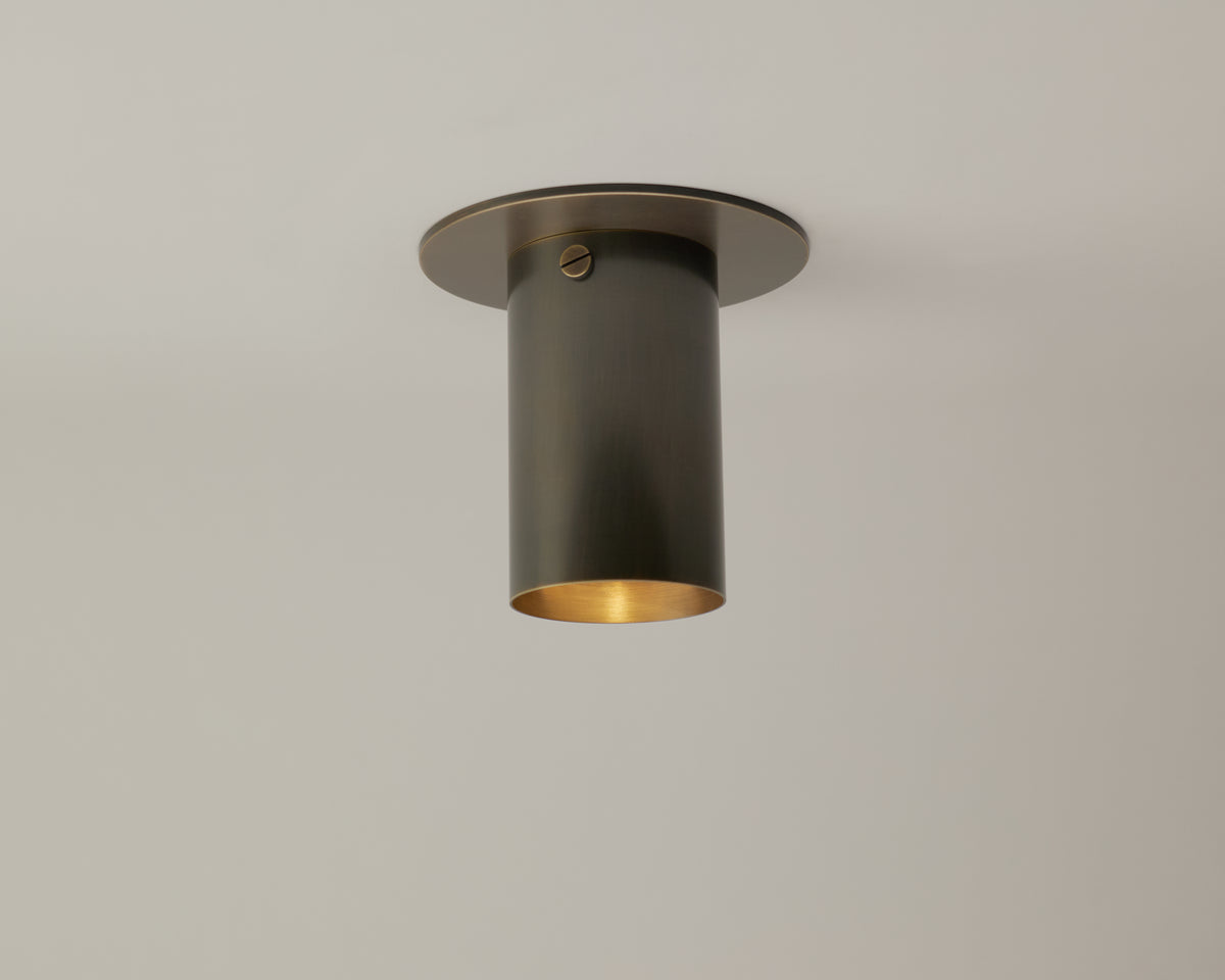The Long Made Co. Brass Cylinder Flush Spot is a modern, matte brass ceiling light mounted flush to a white ceiling, casting a warm downward glow.