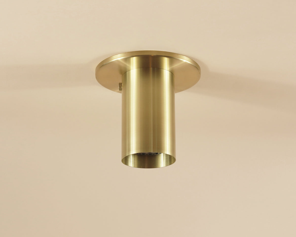 The Brass Cylinder Flush Spot by Long Made Co. is a handmade, minimalist ceiling light with a cylindrical brass body and round base, offering contemporary style inspired by mid-century modern design.