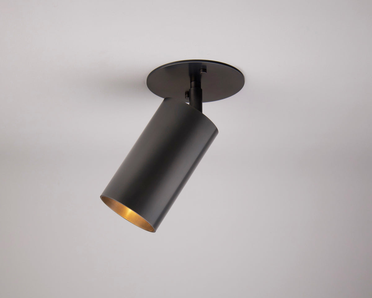 The Highland Adjustable Spot by Long Made Co. is a sleek, cylindrical black ceiling spotlight mounted on a white ceiling, offering minimalist lighting with its adjustable downward beam.