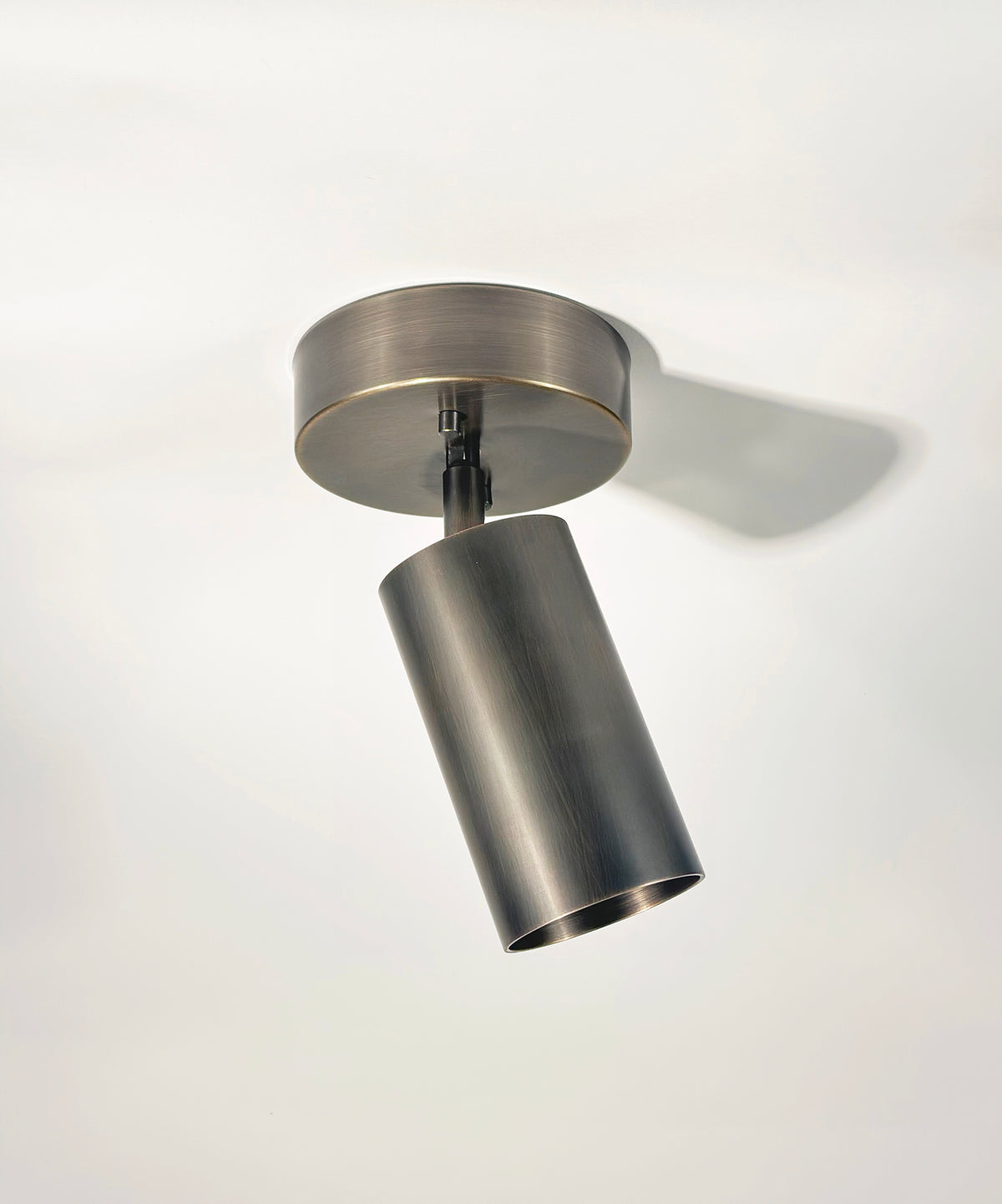 The Highland Adjustable Chunky Spot by Long Made Co. features a modern cylindrical design with a brushed metal finish, angled downward from a round base for sleek, minimalist lighting on any white ceiling.