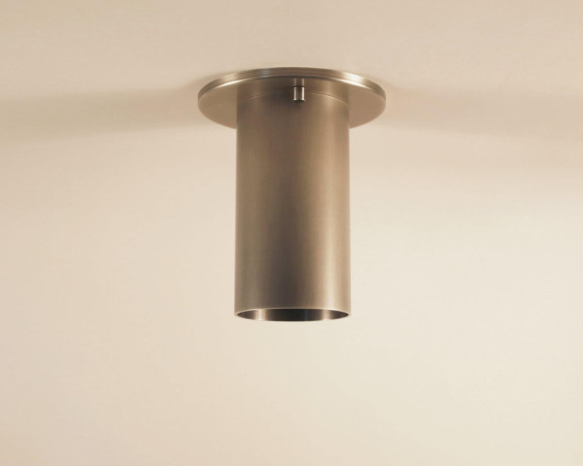 The Highland Flush Spot by Long Made Co. is a modern, cylindrical metal ceiling light with a brushed finish, mounted on an off-white ceiling to showcase the clean elegance of refined flush monopoint lighting.