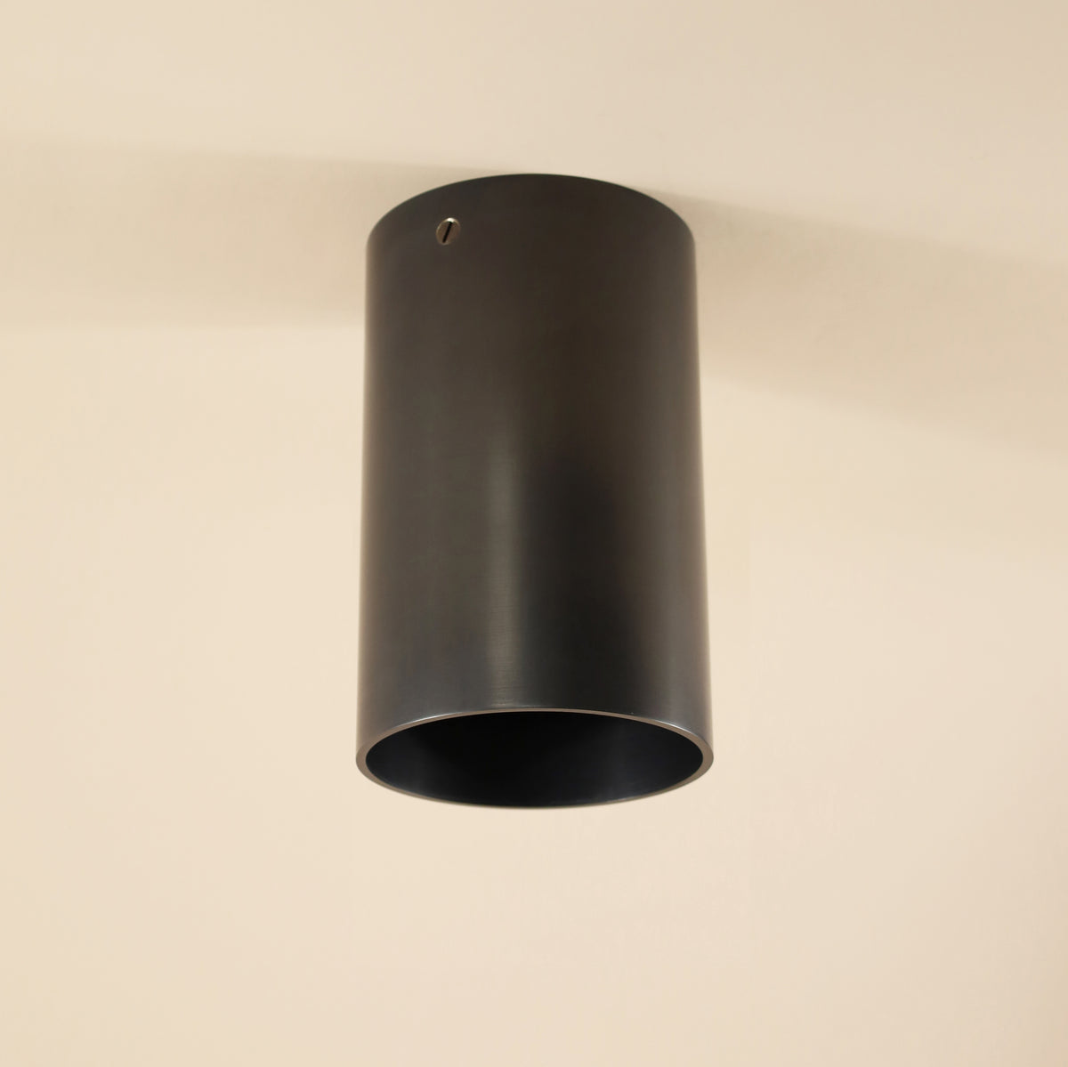 The Long Made Co. Beau Laiton XL Trimless Downlight – Ketra S30 Compatible is a minimalist cylindrical fixture in matte black, seamlessly mounted on an off-white ceiling for modern interiors, with a small hole near the top edge for subtle detail.