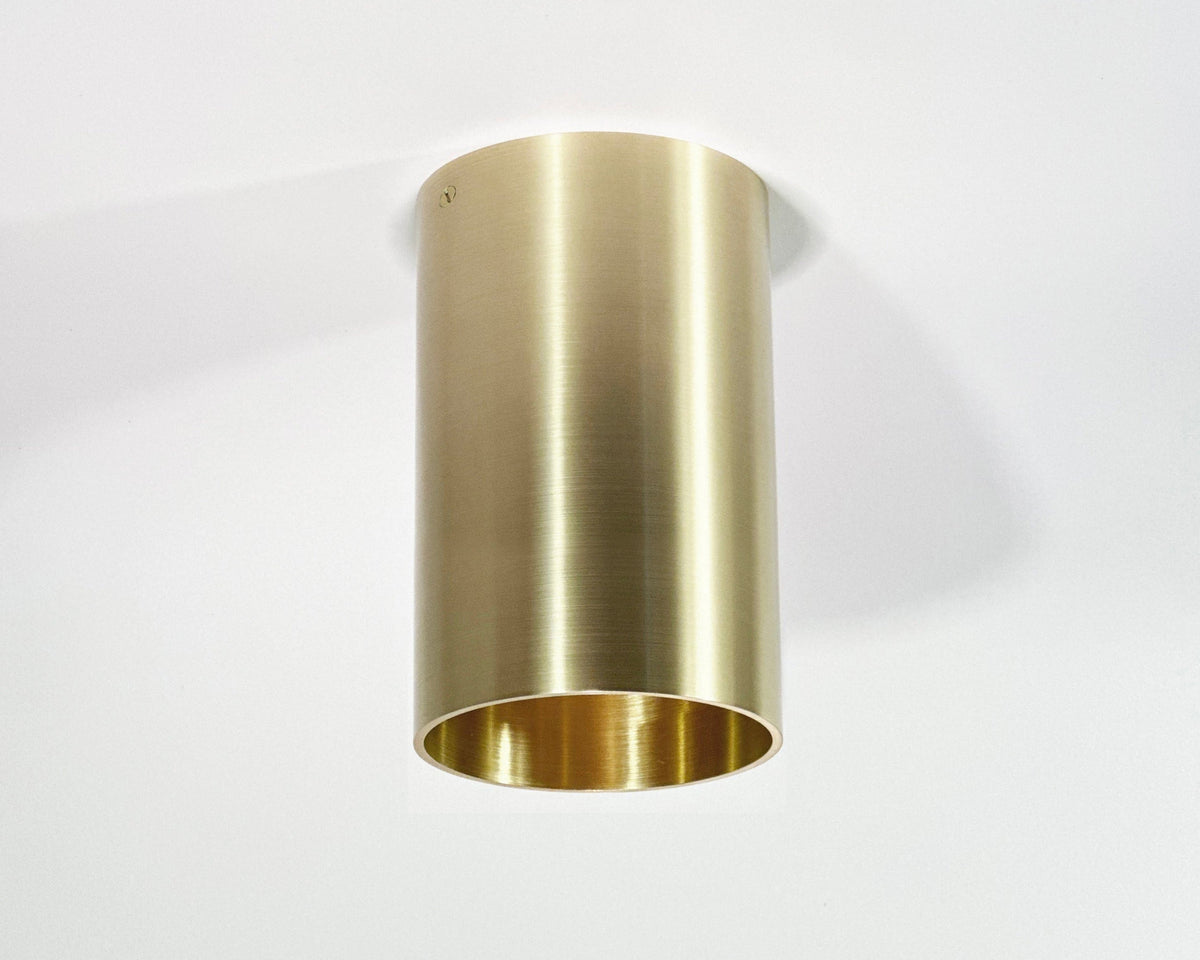 The Beau Laiton XL Trimless Downlight by Long Made Co. features a cylindrical solid brass design with a smooth, brushed finish and is trimlessly mounted on a white ceiling; it’s compatible with Ketra S30 bulbs.