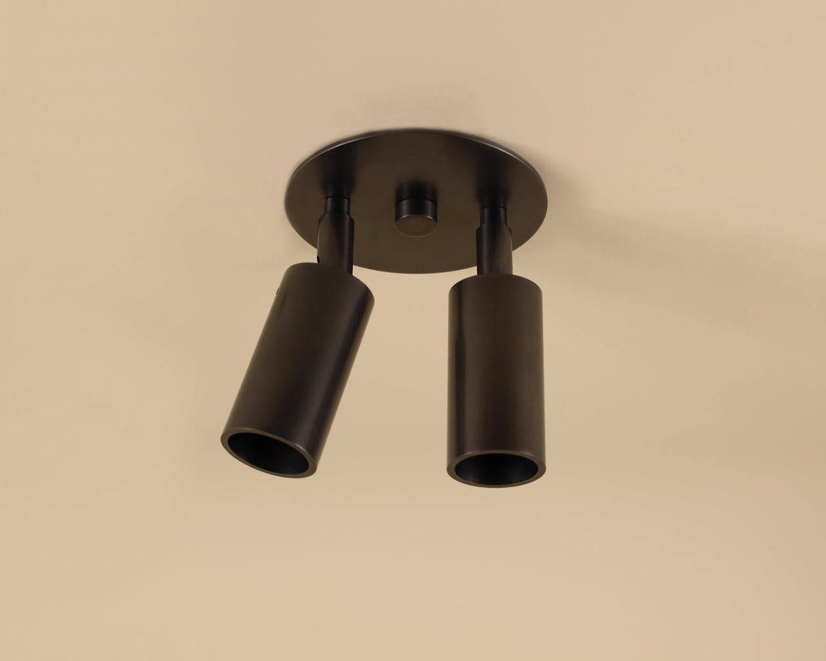 The Long Made Co. Micro Adjustable Spot - Double / Triple is a modern black ceiling light with two adjustable LED cylindrical spotlights hanging from a round base, shown here against a beige ceiling.