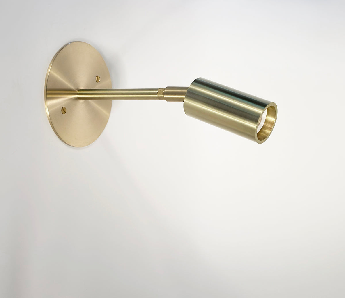 The Micro Wall Spot by Long Made Co. is a modern, ultra-flush wall sconce with a round base and adjustable cylindrical head in brass, featuring a G9 LED spot and set against a plain white background.