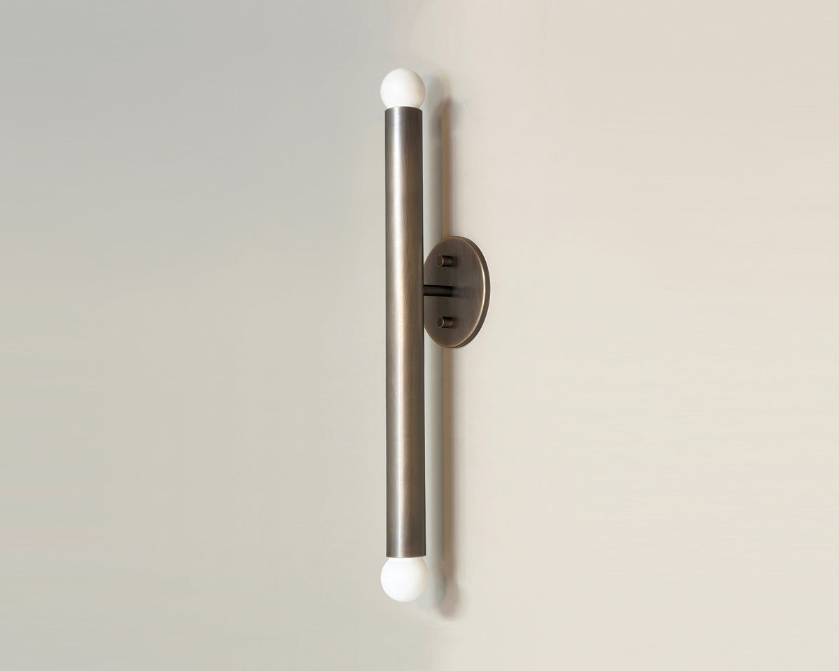 The Miro 2 XXL - 24" Sconce by Long Made Co. is a modern cylindrical brass wall sconce with a brushed metal finish, white globes at both ends, and mounts vertically on a round base.