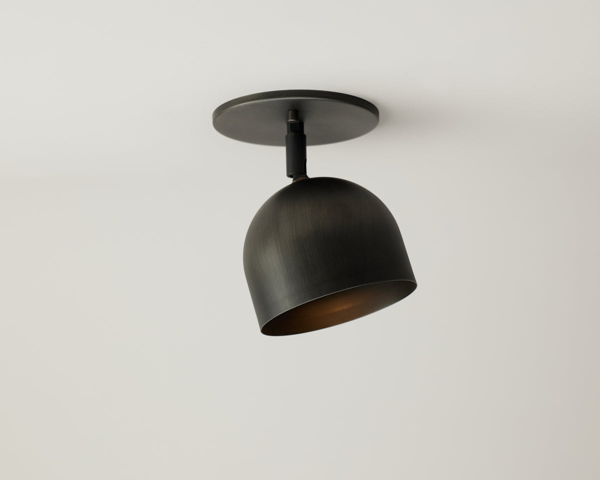 The Long Made Co. Monaco Spot is a modern, dome-shaped black ceiling downlight with solid steel construction, mounted to a white ceiling and featuring an angled lampshade.