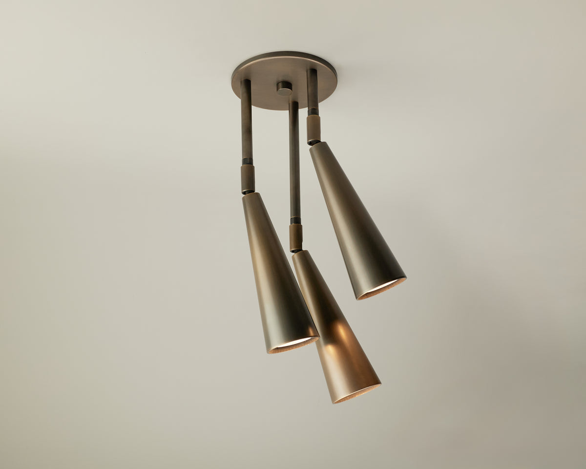 The Long Made Co. Pine Cascade Drop Spot is a solid brass ceiling light featuring three cone-shaped, metallic pendants suspended at varying angles from a round base. Designed for both elegance and versatility, this modern fixture provides adjustable spot lighting to complement any space.