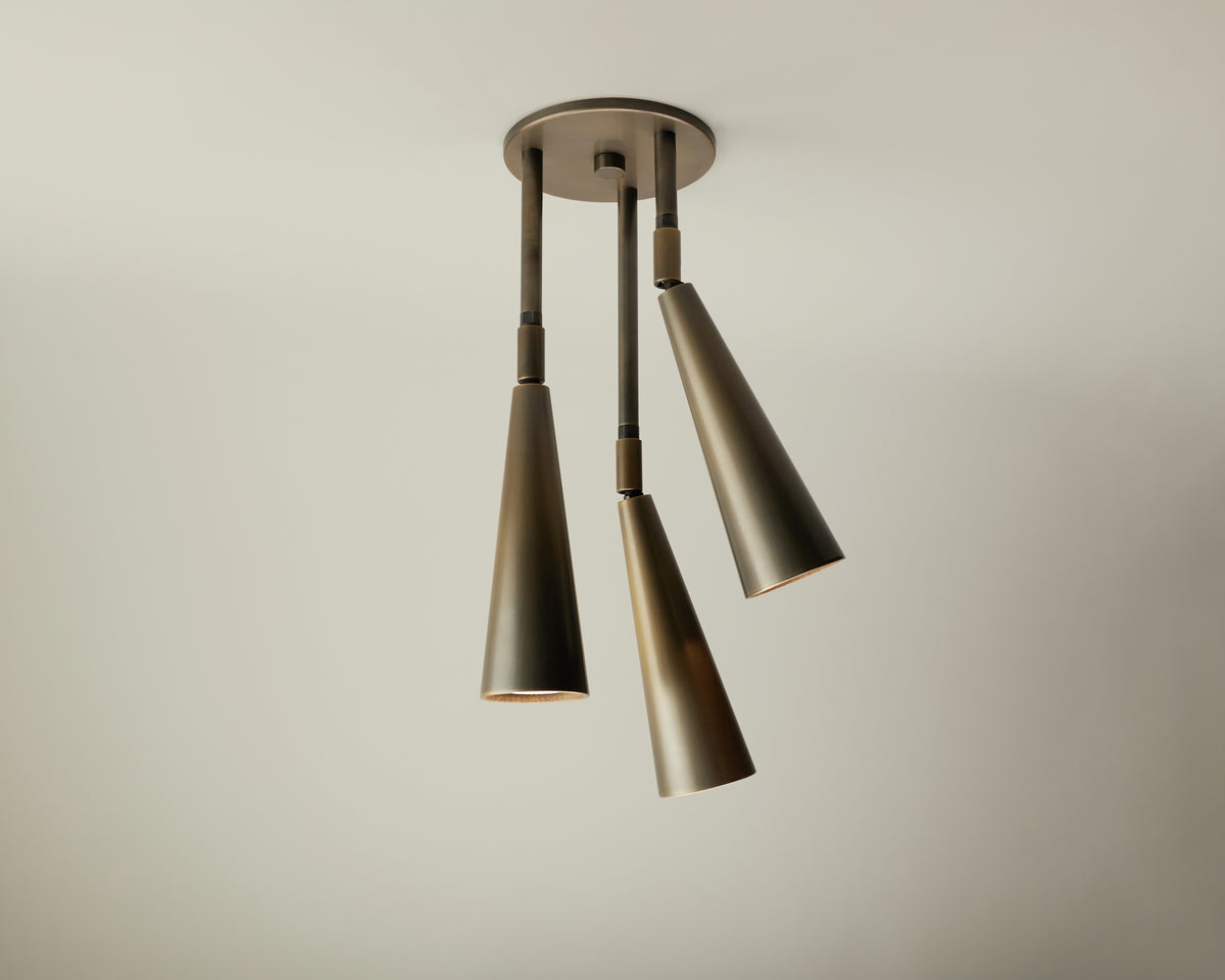 The Pine Cascade Drop Spot by Long Made Co. is a modern ceiling light from the Pine Series, featuring three metallic cone-shaped lamps designed as adjustable spotlights, each suspended at varying angles against a plain light-colored ceiling.