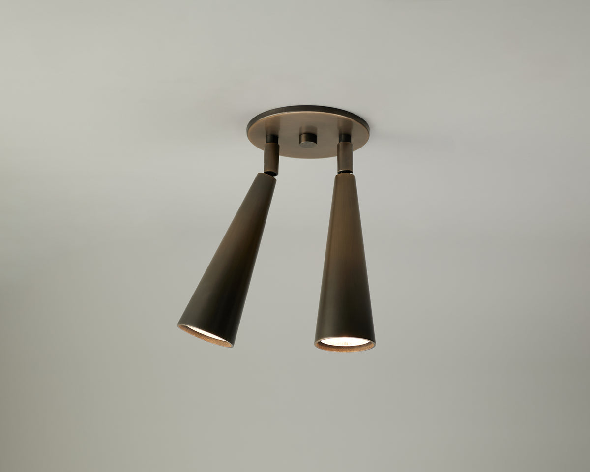 A modern two-light ceiling fixture with tapered dark metal shades and a circular ceiling mount, shown against a plain light gray wall.