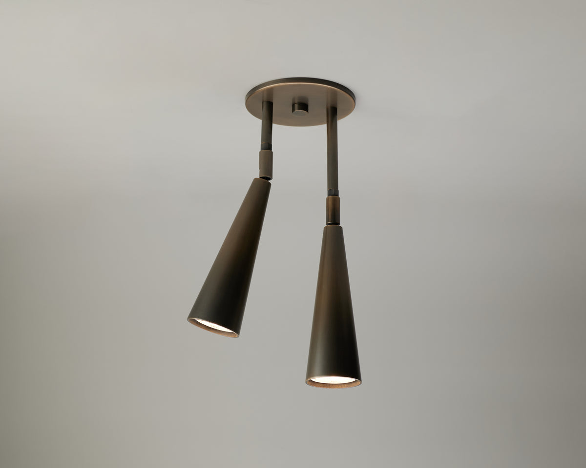 The Pine Double Drop Spot by Long Made Co. is a modern ceiling light fixture featuring two black, cone-shaped adjustable spot head downlights attached to a round base, providing focused illumination against a plain gray ceiling.