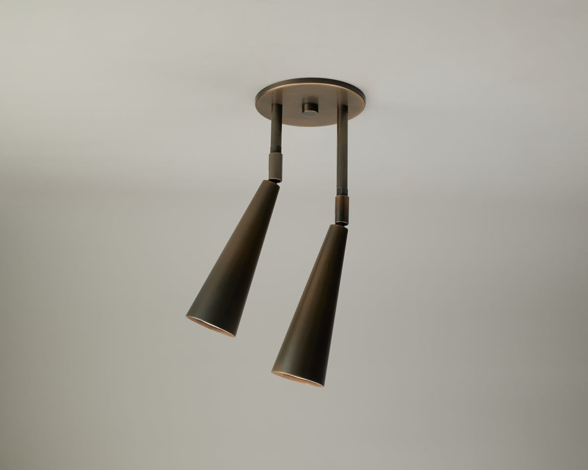 Two black, cone-shaped Pine Double Drop Spot pendant lights by Long Made Co. are suspended from a circular ceiling mount against a plain, light-colored background, providing an elegant lighting solution ideal for vaulted ceilings.