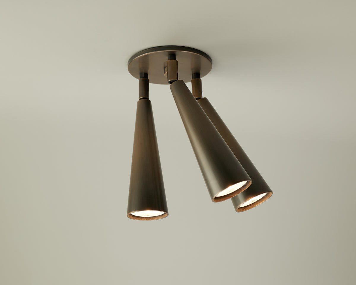 A Long Made Co. Pine Double / Triple Spot ceiling light fixture from the Pine Series lights collection features three adjustable spot heads with cone-shaped, bronze-colored metal shades, each directed differently and mounted on a round base against a plain white ceiling.