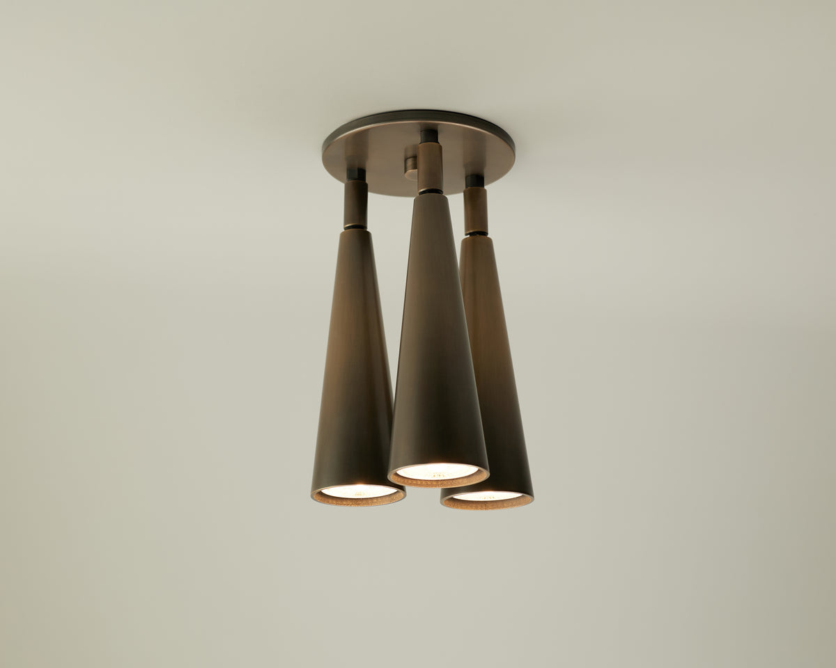 A modern ceiling light fixture from Long Made Co.’s Pine Double / Triple Spot collection, featuring three downward-facing, cone-shaped bronze lamps with adjustable spot heads set against a plain light-colored ceiling.