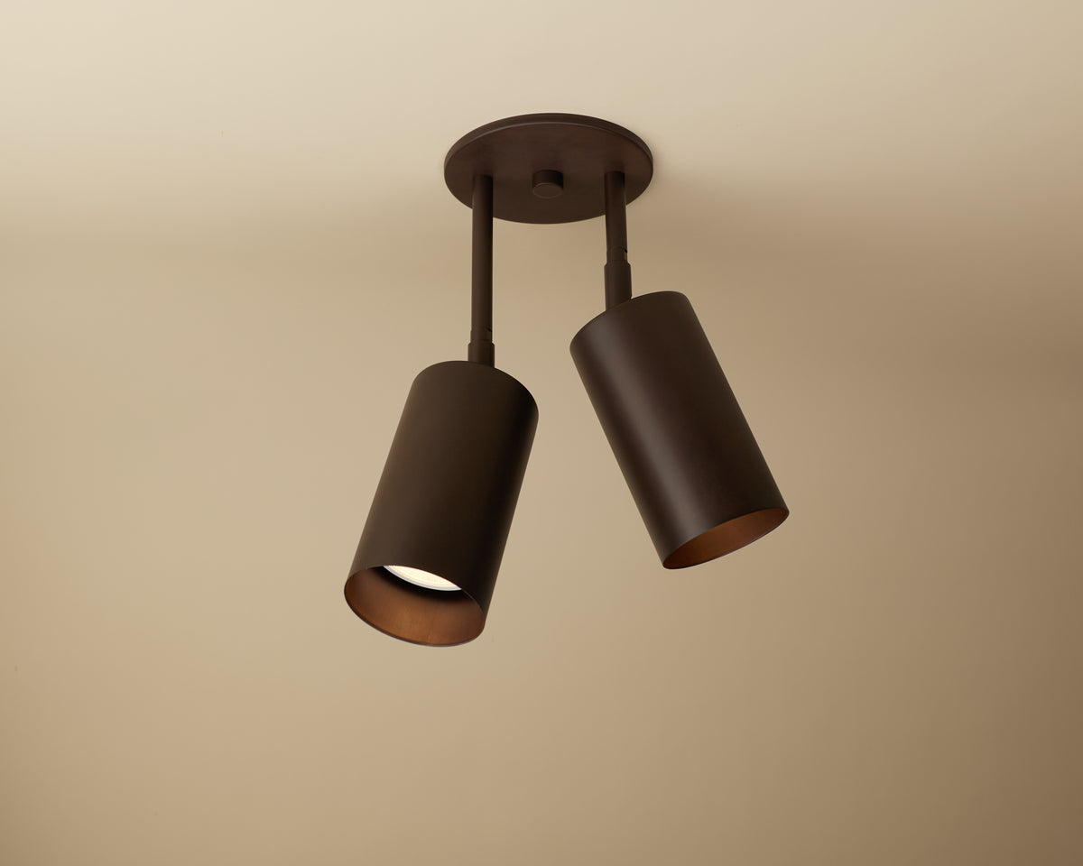 The Cove Double Drop Spot by Long Made Co. is a modern, adjustable ceiling downlight with two solid steel spotlights on a round base, offering versatile, minimalist lighting with one angled downward and the other slightly to the side.