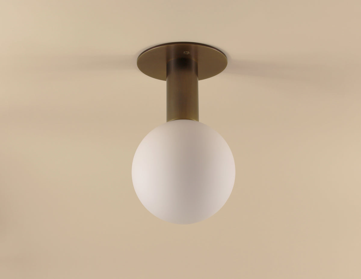 The Sphere Drop by Long Made Co. is a modern ceiling light featuring a matte glass globe and solid brass flush mount, elegantly installed on a beige ceiling.