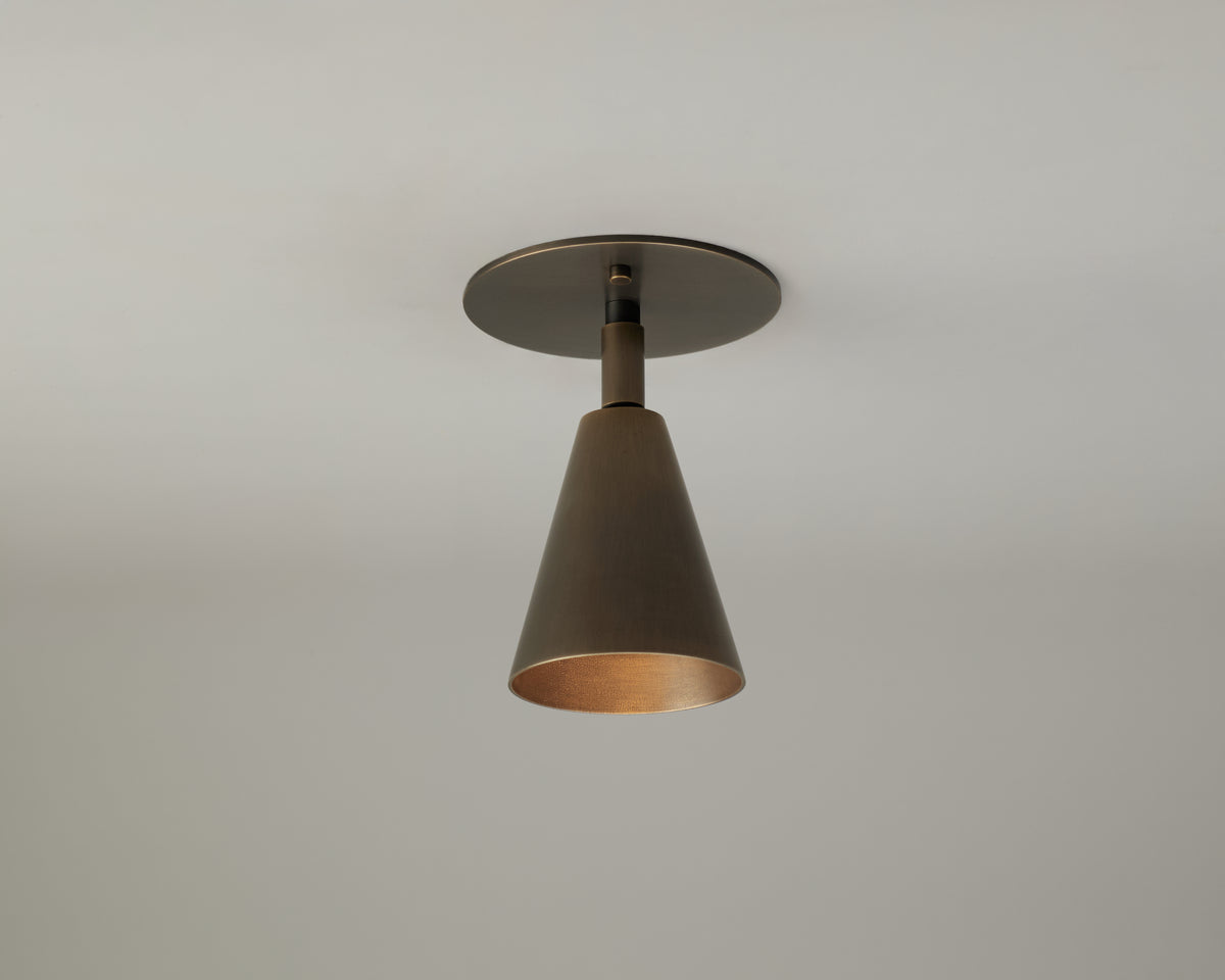 A single Tiel Adjustable Spot ceiling light fixture by Long Made Co. is mounted on a white ceiling, casting a warm downward glow as a stylish alternative to traditional recessed can lights.