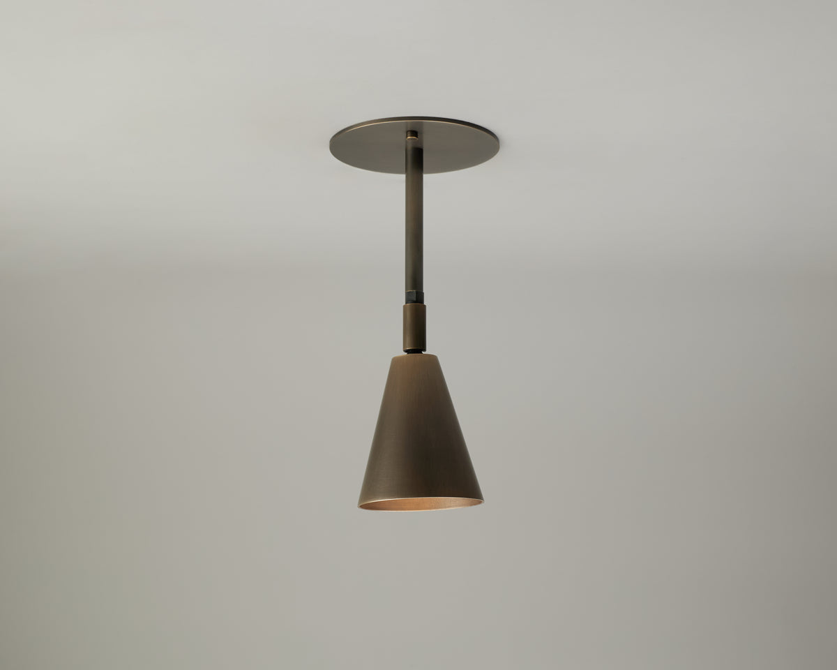 A single Tiel Drop Spot pendant light fixture by Long Made Co., featuring a modern bronze finish and suspended from a round ceiling mount, is displayed against a plain light gray background.