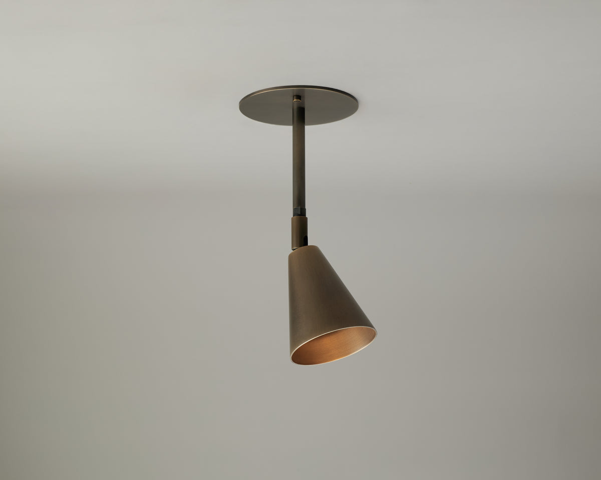 The Tiel Drop Spot by Long Made Co. is a contemporary solid brass ceiling light fixture featuring a cone-shaped shade, suspended from a white ceiling against a plain, light-colored background—offering stylish directional downlight ideal for modern interiors.