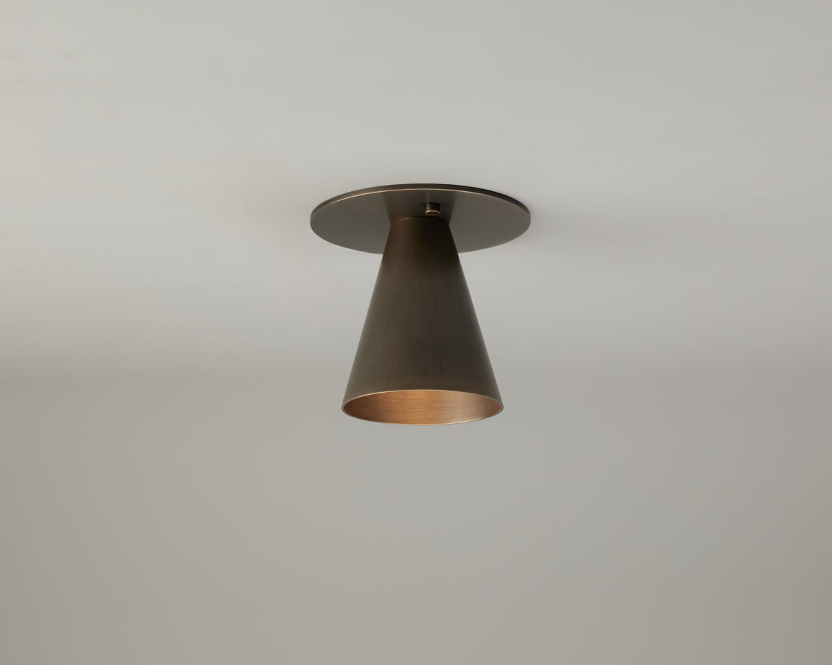A single, modern Tiel Flush Spot ceiling light fixture by Long Made Co., featuring a sleek cone-shaped metallic design, is installed flush in a minimalist style on a plain white ceiling. The light is off.