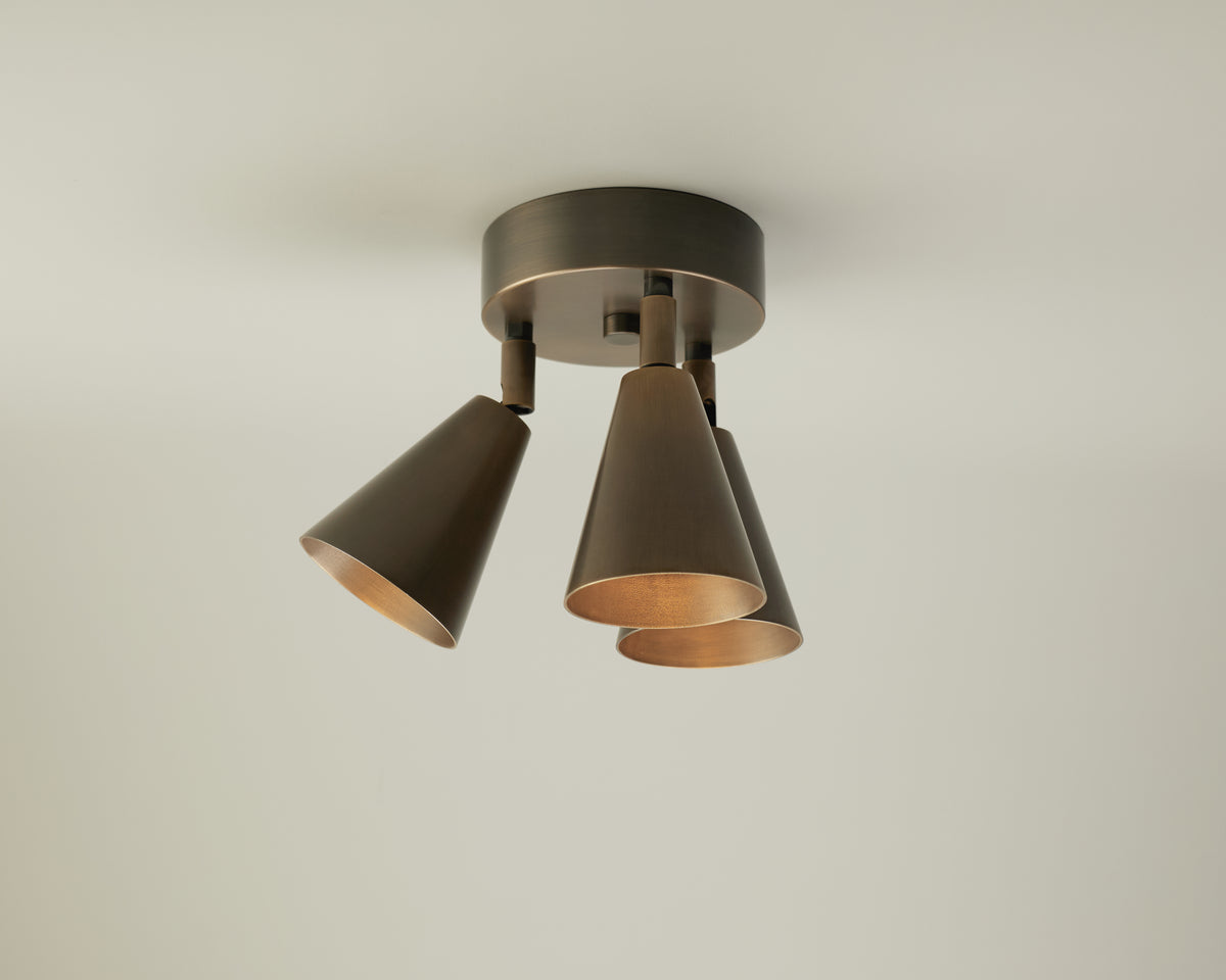 The Tiel Triple Spot by Long Made Co. is a modern ceiling light fixture featuring three bronze-finished, conical lampshades arranged evenly in a circular layout, offering sleek directional downlighting—an ideal mid-century-inspired choice for neutral ceilings.