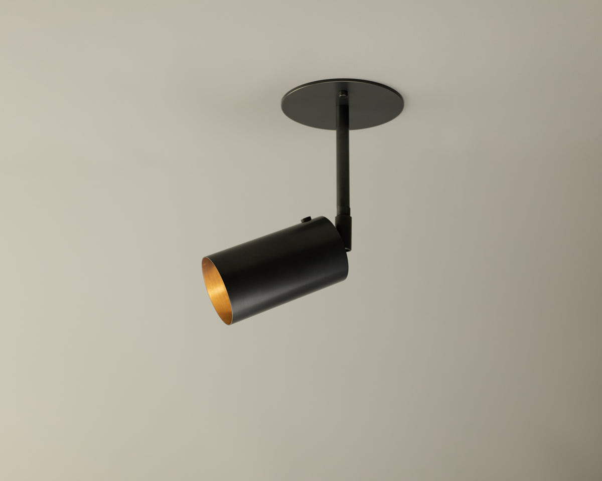 The Brass Cylinder Drop Spot - Top Mount by Long Made Co. is a cylindrical brass directional ceiling light with a round base, casting focused downward illumination—ideal for enhancing mid-century modern lighting schemes.