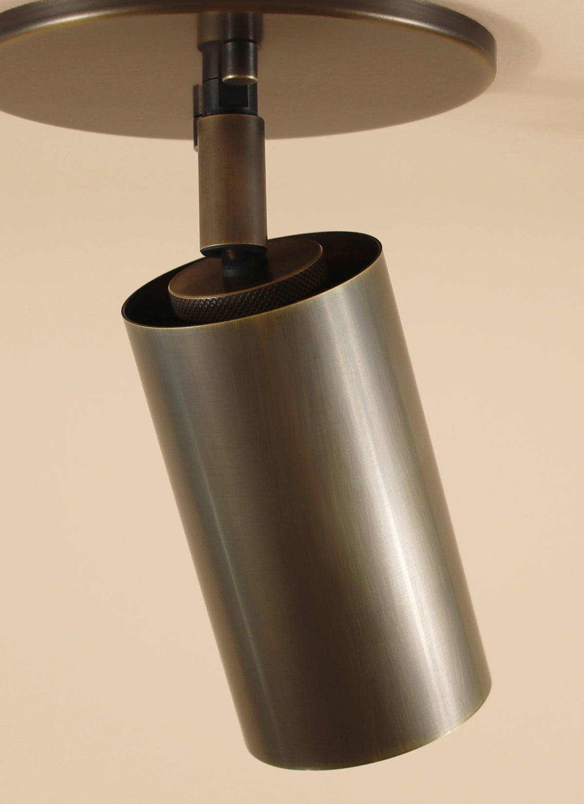 The Long Made Co. Brass Cylinder Adjustable Spot - Top Mount is a modern, minimalist brushed metal ceiling spotlight with a cylindrical design, mounted on a round base for directional downlighting against light-colored ceilings.
