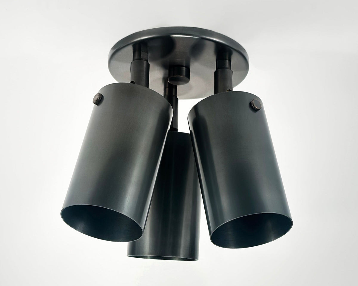 A brass cylinder triple or double spot ceiling light fixture with adjustable heads, designed for true vertical and horizontal positions and 330-degree rotation.