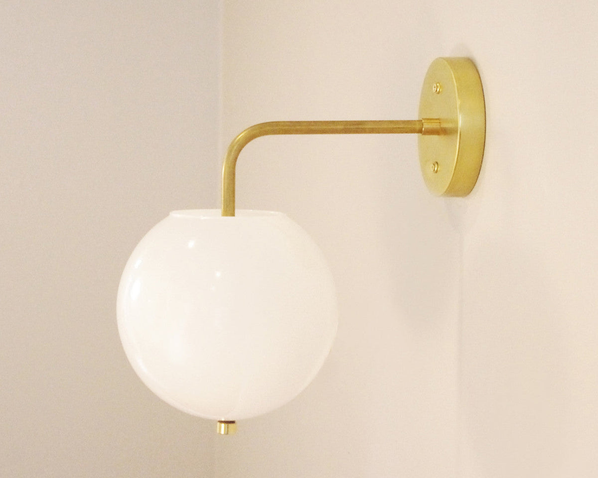 The Wade Wall 8" Globe by Long Made Co. is a modern handmade brass wall sconce with a round frosted glass shade and brass arm, elegantly displayed on a light-colored wall.