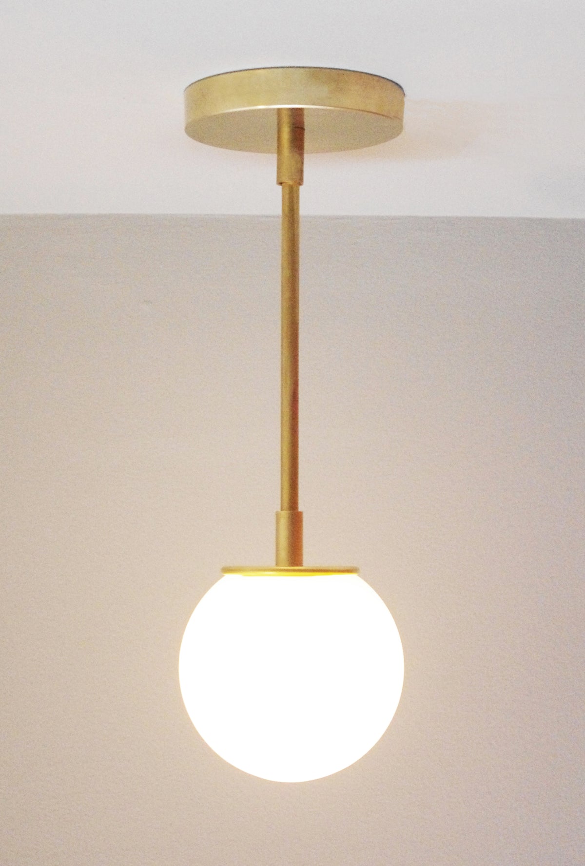 The Sphere Solo Drop - 10" by Long Made Co. features a solid brass pendant and opal glass shade, softly illuminating neutral walls and ceilings with elegant, handmade style.