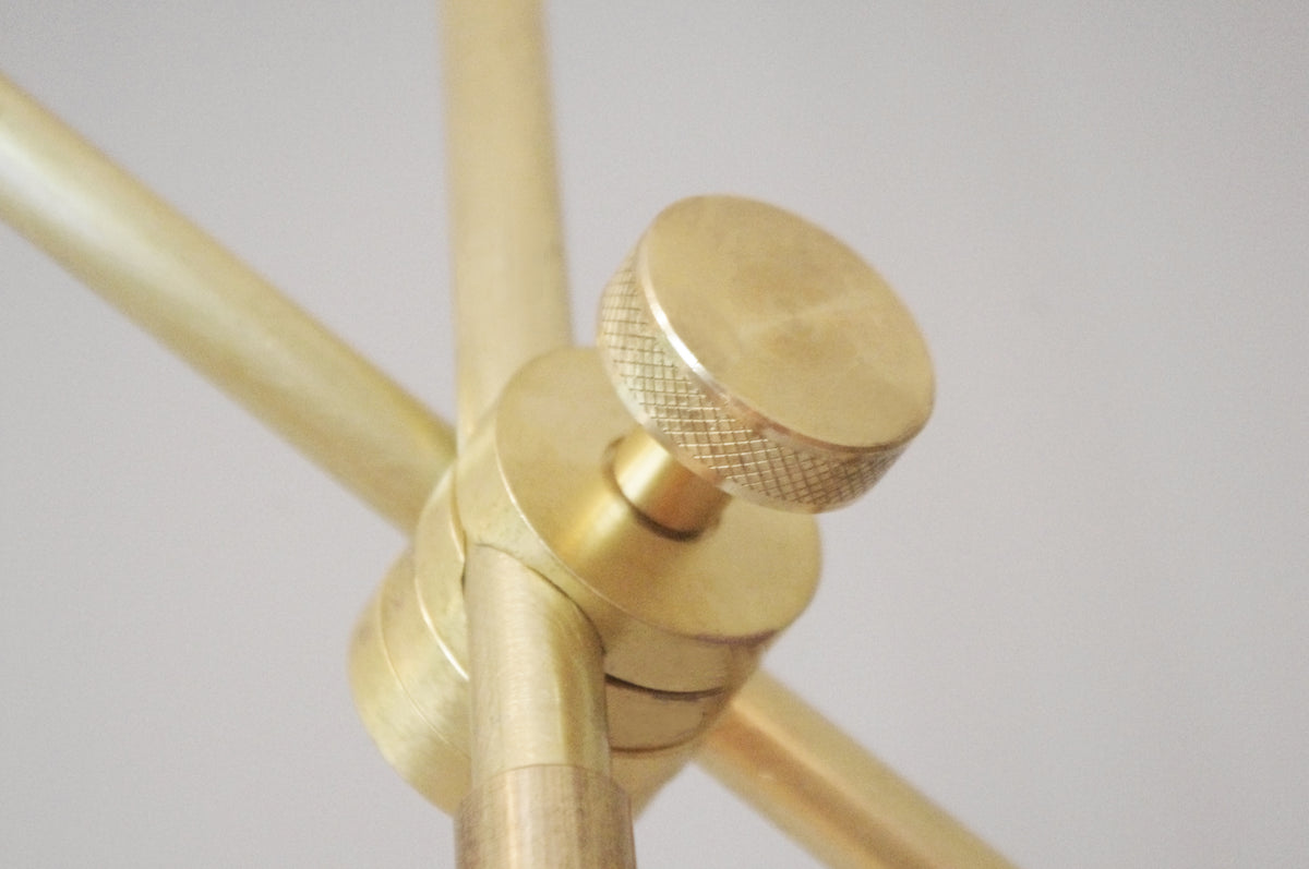 Close-up of a brass knurled screw joining metal rods on the Task Articulating Chandelier by Long Made Co., showcasing its minimalist, industrial design against a plain background.