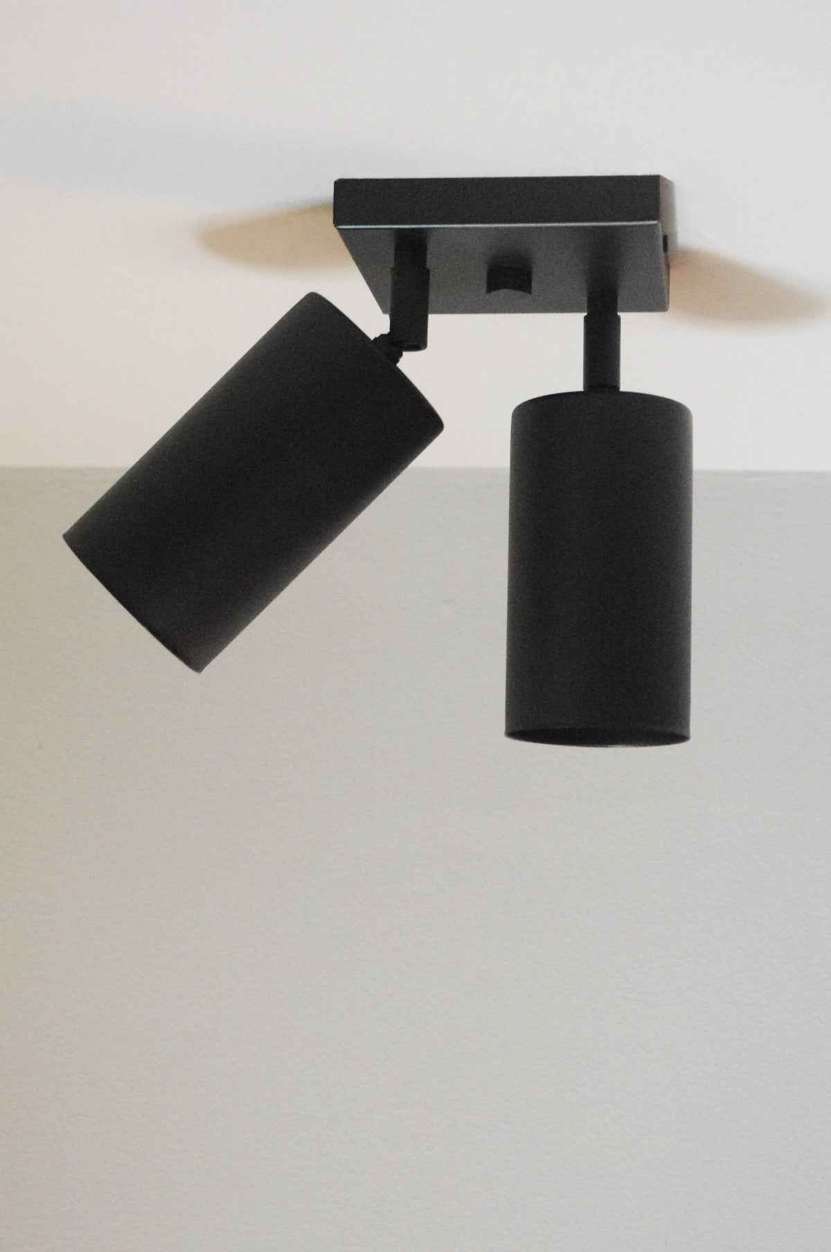 The Cove Double Spot by Long Made Co. is a modern black directional ceiling downlight with two solid steel spotlights on a square base for sleek, minimalist lighting.