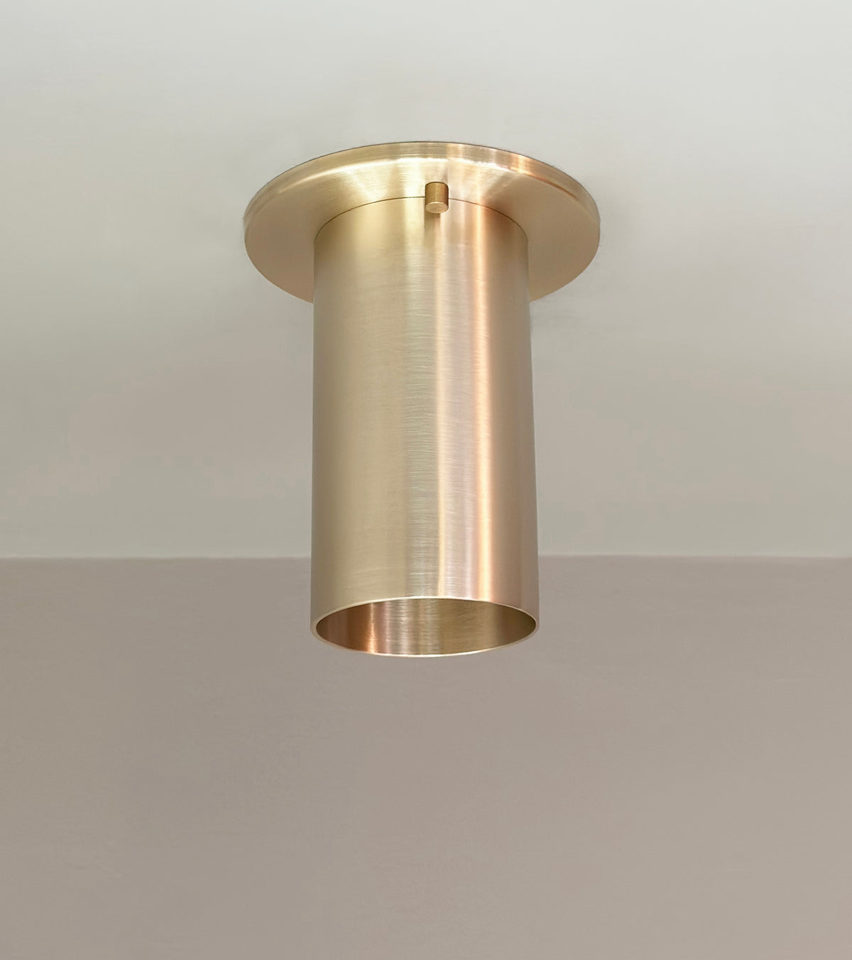 The Highland Flush Spot by Long Made Co. is a cylindrical brass ceiling light with a brushed metal finish, handmade in Texas and flush-mounted for a sleek look on any white ceiling.