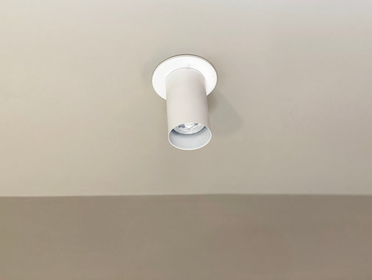 A white, cylindrical Cove Flush Spot ceiling spotlight by Long Made Co. is mounted on a plain, light-colored ceiling. The minimalist fixture is turned off, with a simple background and minimal shadows.