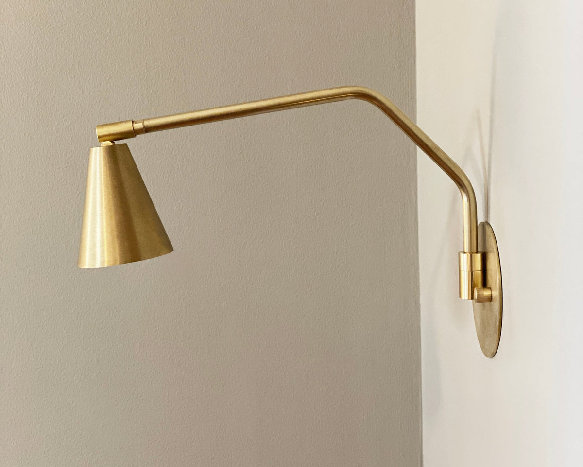 A wall-mounted brass task lamp with an adjustable shade, shown in a natural lighting setting.