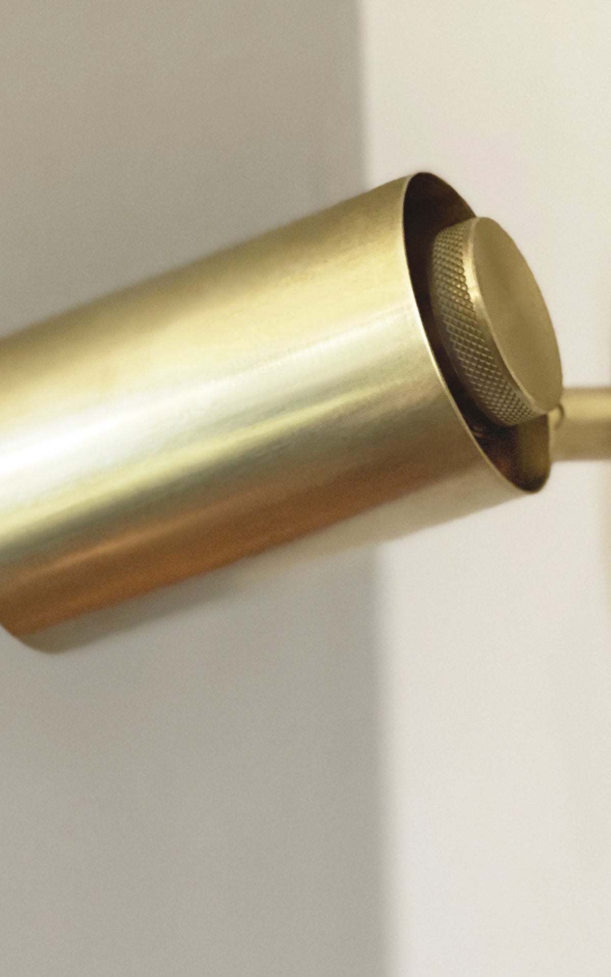 Close-up of the Brass Cylinder Extension Wall Lamp by Long Made Co., a handmade brass sconce with a cylindrical design and textured knob, mounted on a white wall.