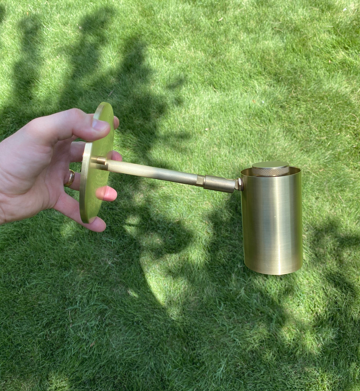 A hand holds the Long Made Co. Brass Cylinder Extension Wall Lamp, a handmade sconce with a sleek cylindrical brass design.