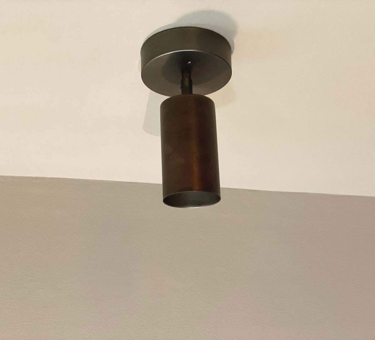 The Cove Adjustable Chunky Spot by Long Made Co., a modern cylindrical black solid steel downlight from the Cove Series, is mounted on a white ceiling with part of a beige wall visible below.