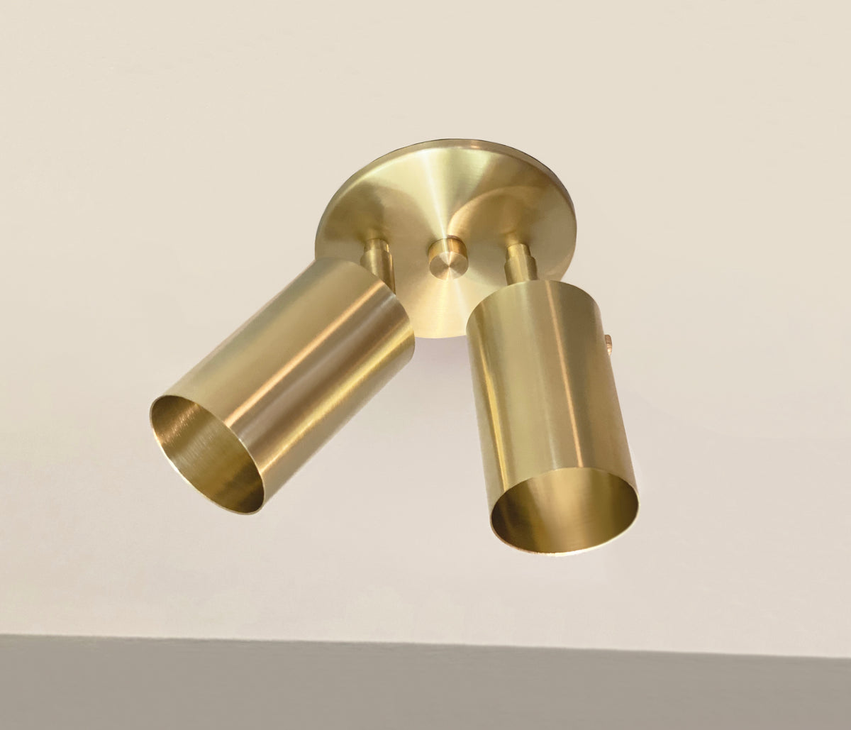 The Long Made Co. Brass Cylinder Double Spot is a brass-colored, mid-century modern fixture with two adjustable cylindrical shades on a round base, mounted on a white ceiling.