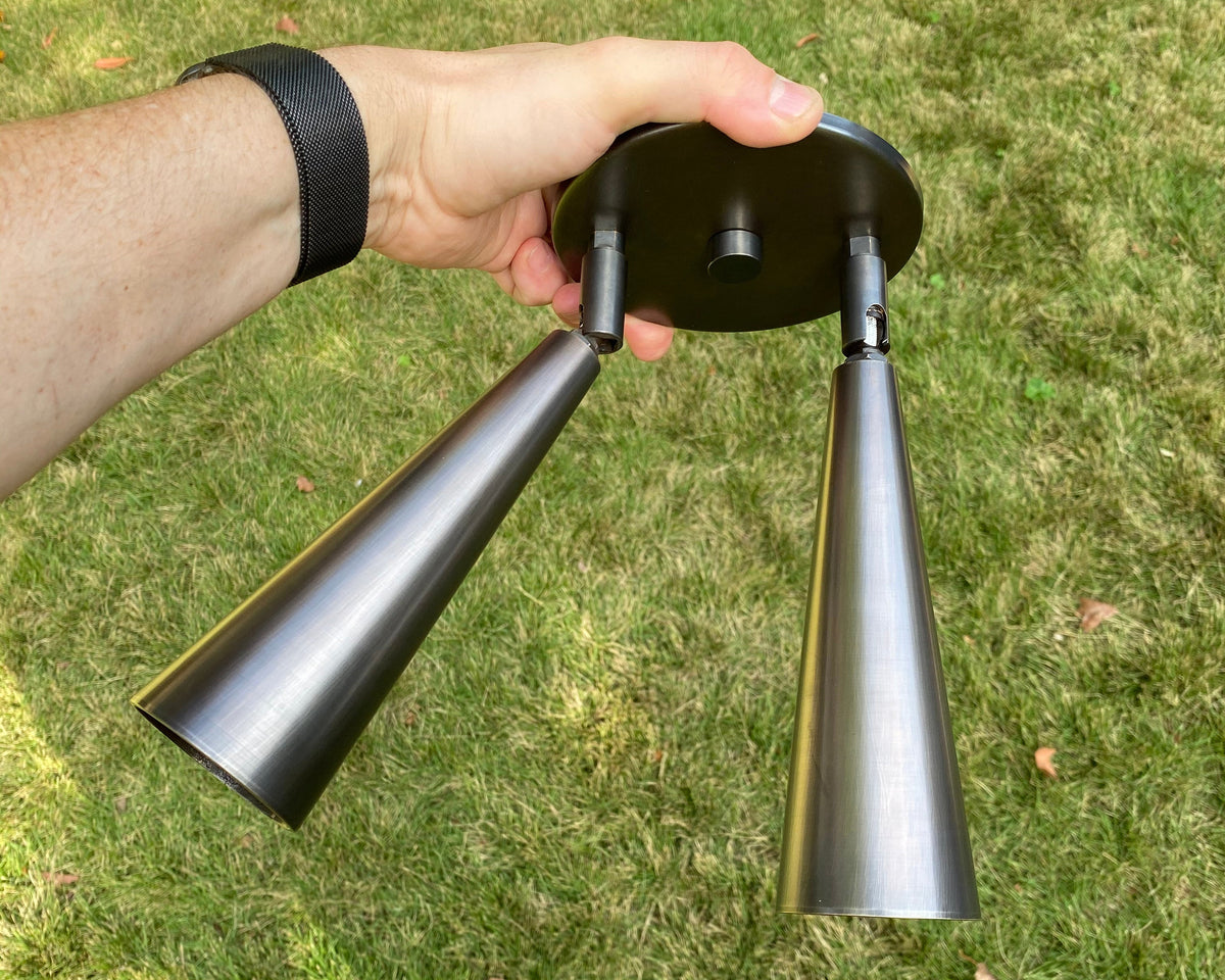 Someone holds the Long Made Co. Pine Double / Triple Spot light fixture, featuring adjustable metal spot heads, outdoors above a grassy lawn.