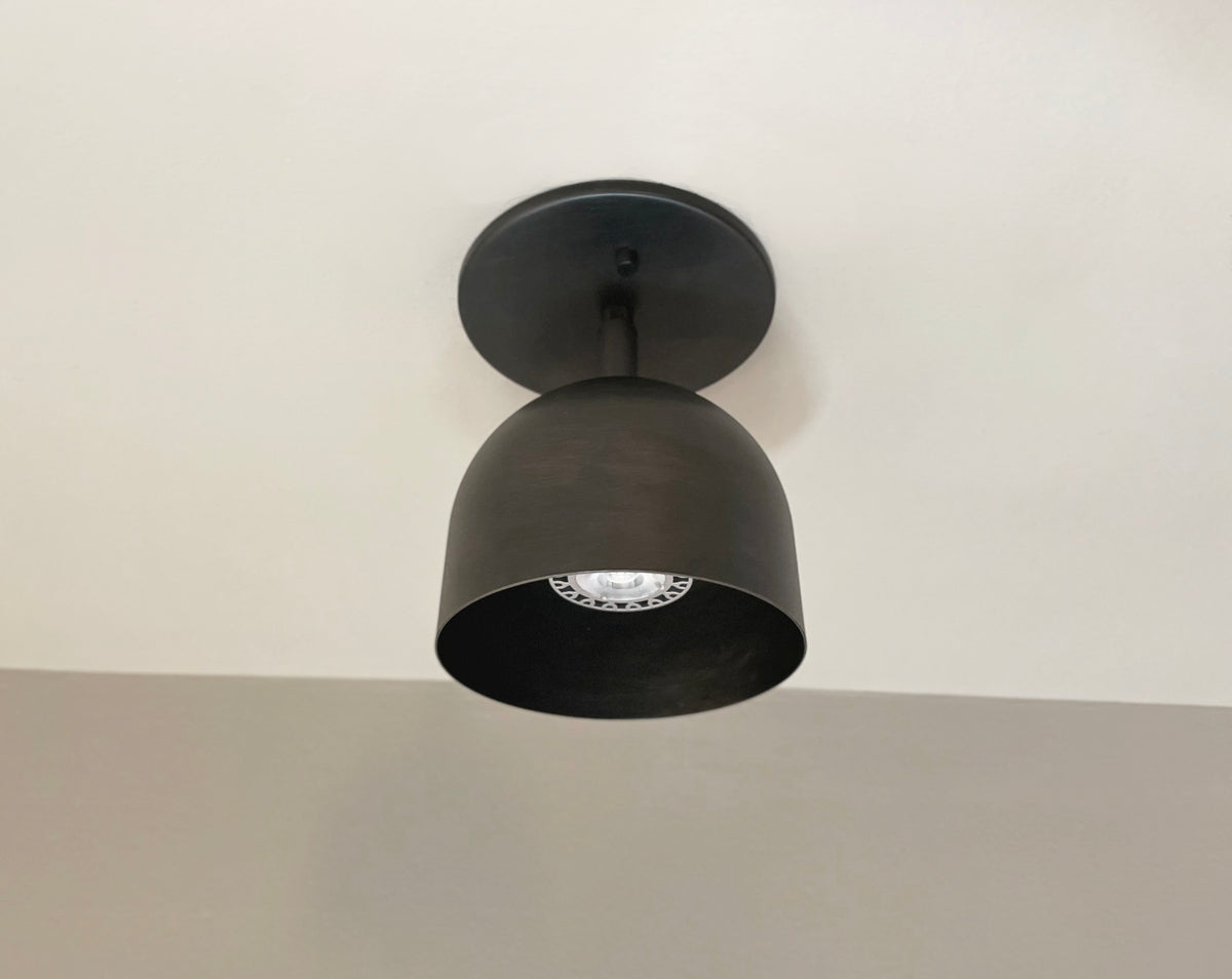 The Monaco Spot by Long Made Co. is a black, dome-shaped downlight with solid steel construction, mounted on a white ceiling and showcasing the light bulb inside its shade.
