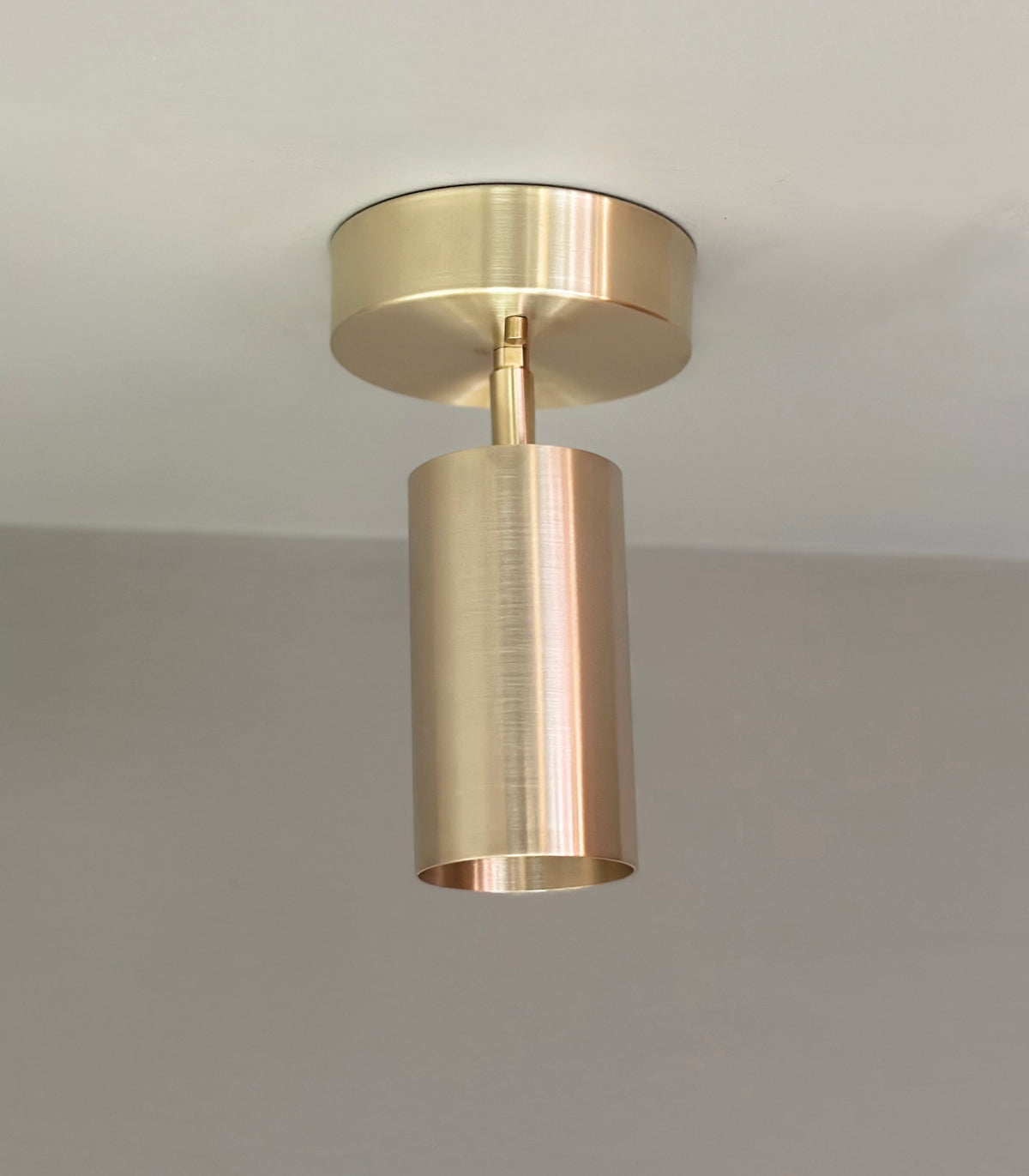 The Highland Adjustable Chunky Spot by Long Made Co. is a modern brass ceiling light with a cylindrical design, flush-mounted on a white ceiling. Its brushed metal finish and minimalist style offer a sleek, contemporary look from the Highland Series.