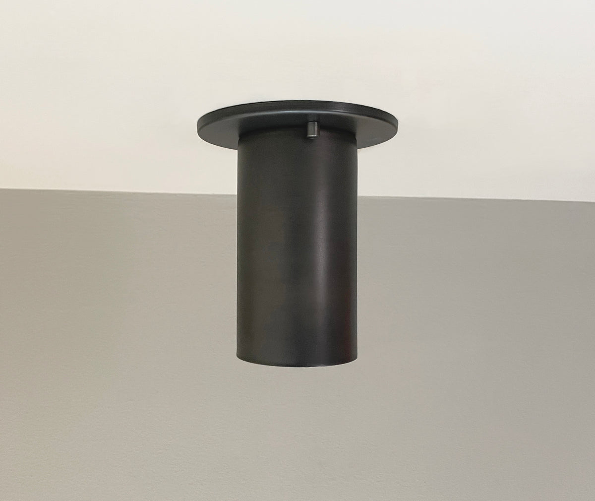 The Cove Flush Spot by Long Made Co. is a modern cylindrical solid steel downlight, mounted on a white and gray wall. With clean lines and an industrial design, it provides ideal task lighting for contemporary spaces.