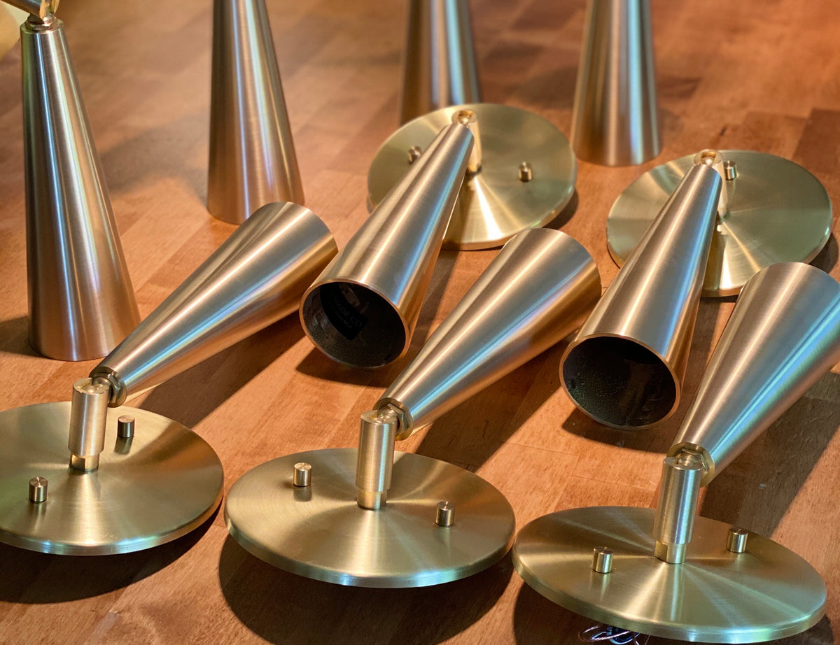 Several gold-colored, cone-shaped metal objects with round bases from Long Made Co.'s Pine Adjustable Spot collection are arranged on wood. These pieces resemble parts for a custom brass ceiling light or directional downlight.